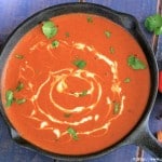 Makhani Gravy in a cast iron pan with tomatoes, red dried chilis, cilantro, cloves and cinnamon