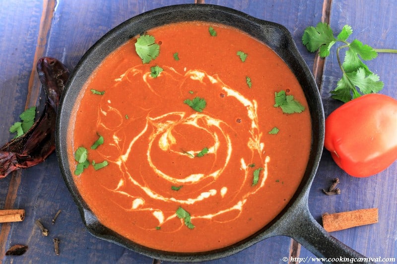 Makhani Gravy in a cast iron pan with tomatoes, red dried chilis, cilantro, cloves and cinnamon