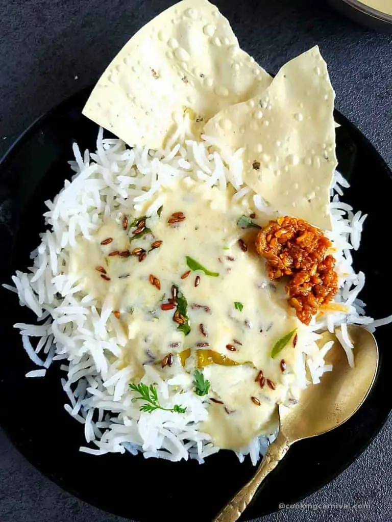 Kadhi bhat, pickle and papad in a black plate