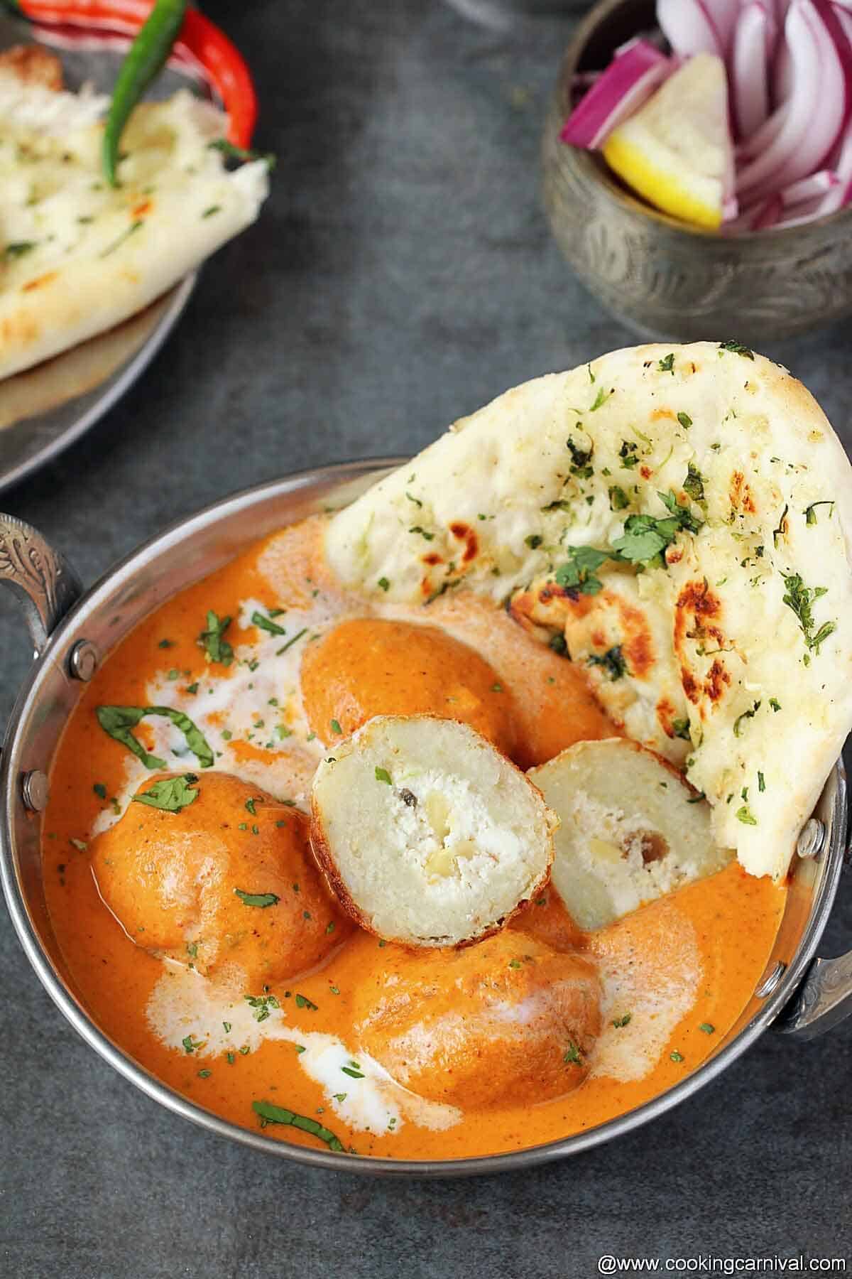 Potato balls dunked in tomato onion based silky gravy, served in steel bowl with naan