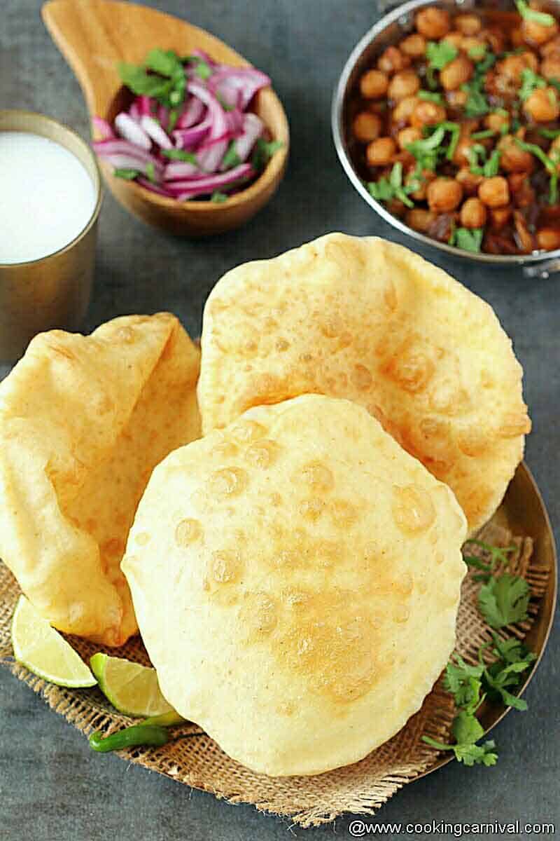 3 bhature in kansa plate, chole, pickle and onion on the side