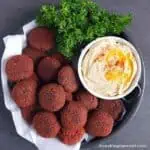 Beetroot falafel served in a plate, with hummus and parsley.