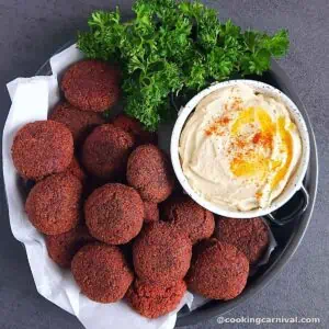 Beetroot falafel served in a plate, with hummus and parsley.