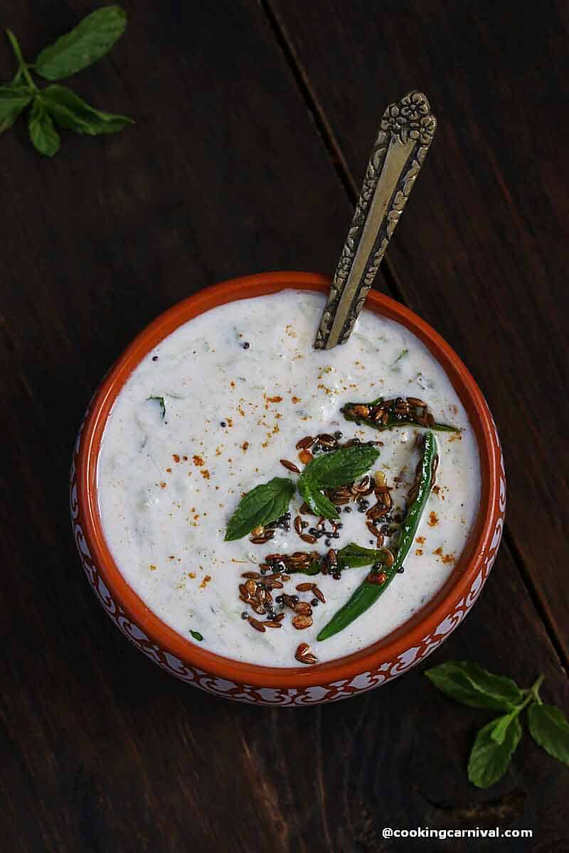 Indian yogurt sauce, cucumber raita in a traditional bowl with spoon.