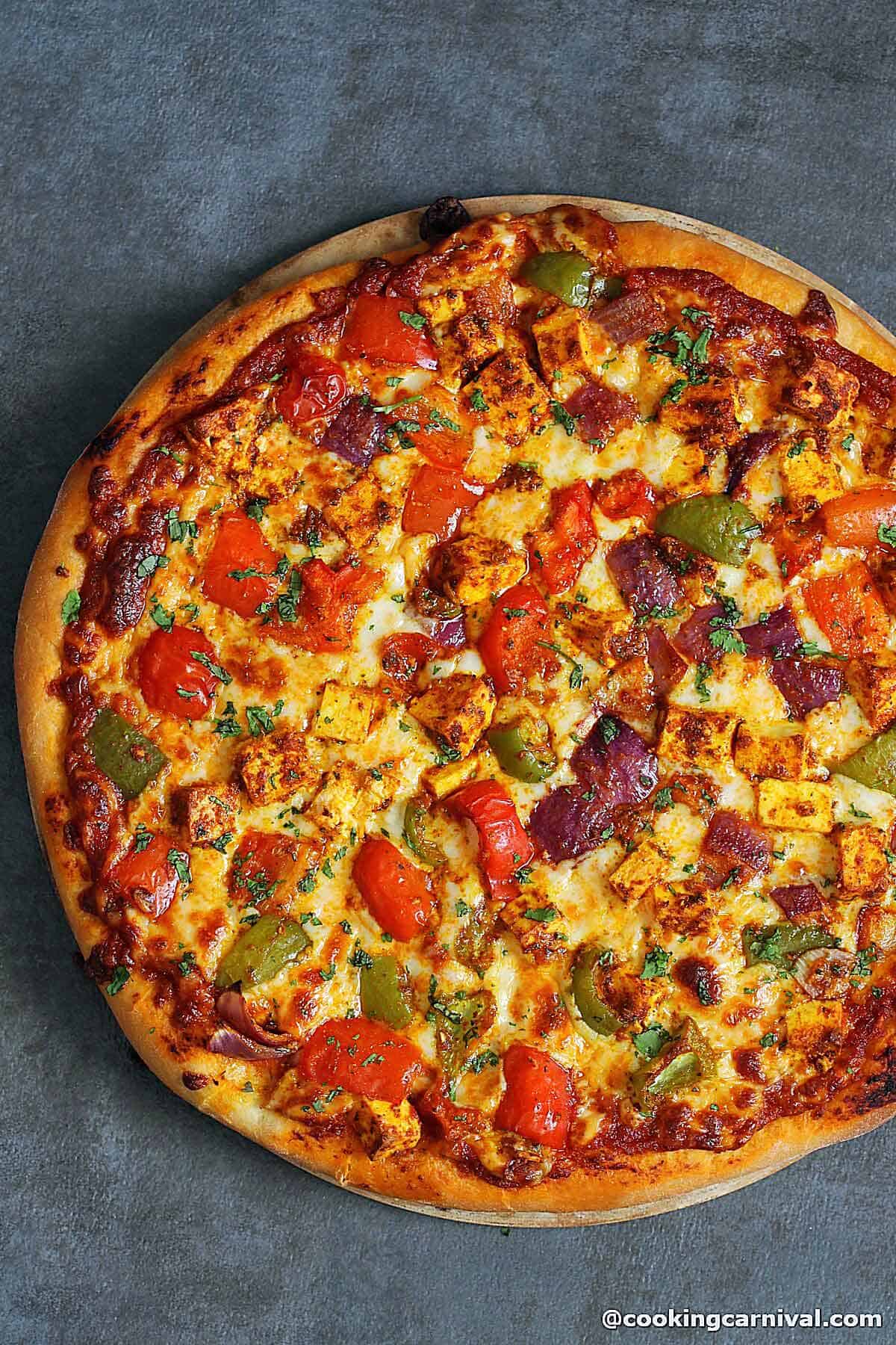 A pizza made with paneer, onion and bel pepper.