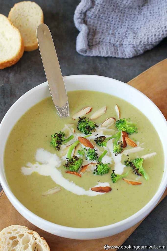 Broccoli almond soup garnished with whipping cream, roasted broccoli and almons, served in white bowl