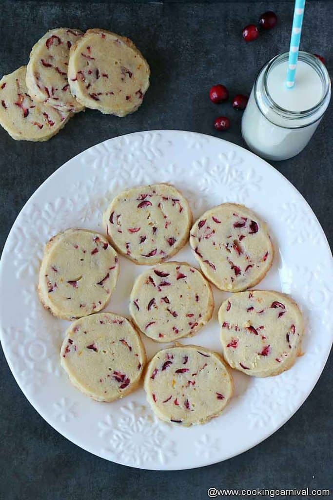 Orange cranberry shortbread cookies in a white plate, milk on the sides