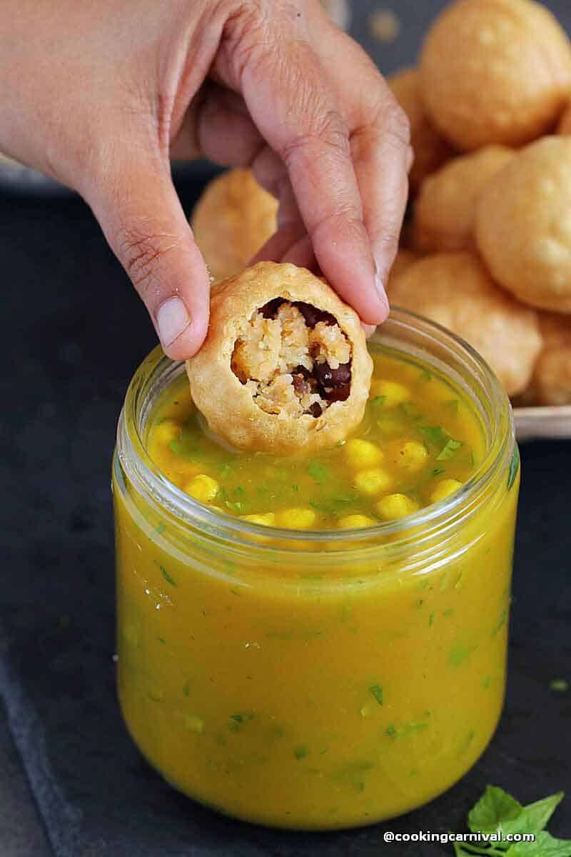 dipping puri filled with potato masala in pani puri ka pani