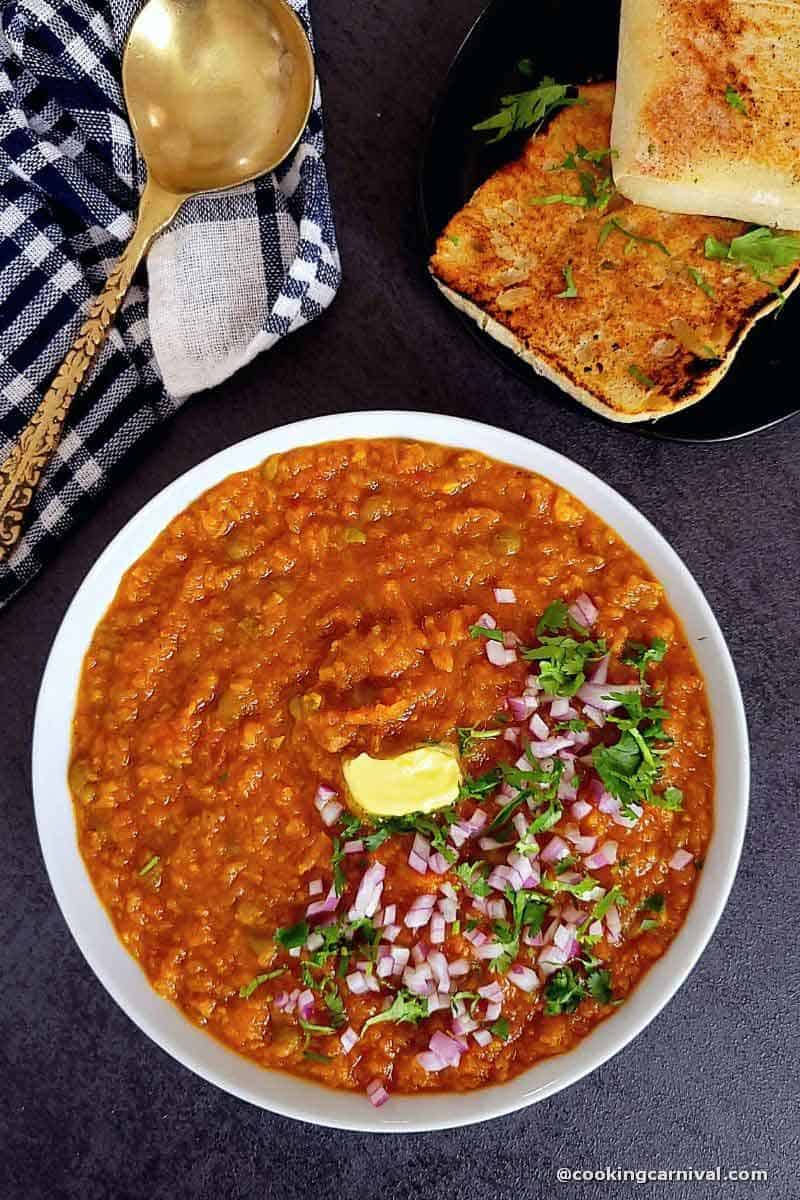 Instant pot pav bhaji served in white bowl, garnished with butter, cilantro, onion and pav.