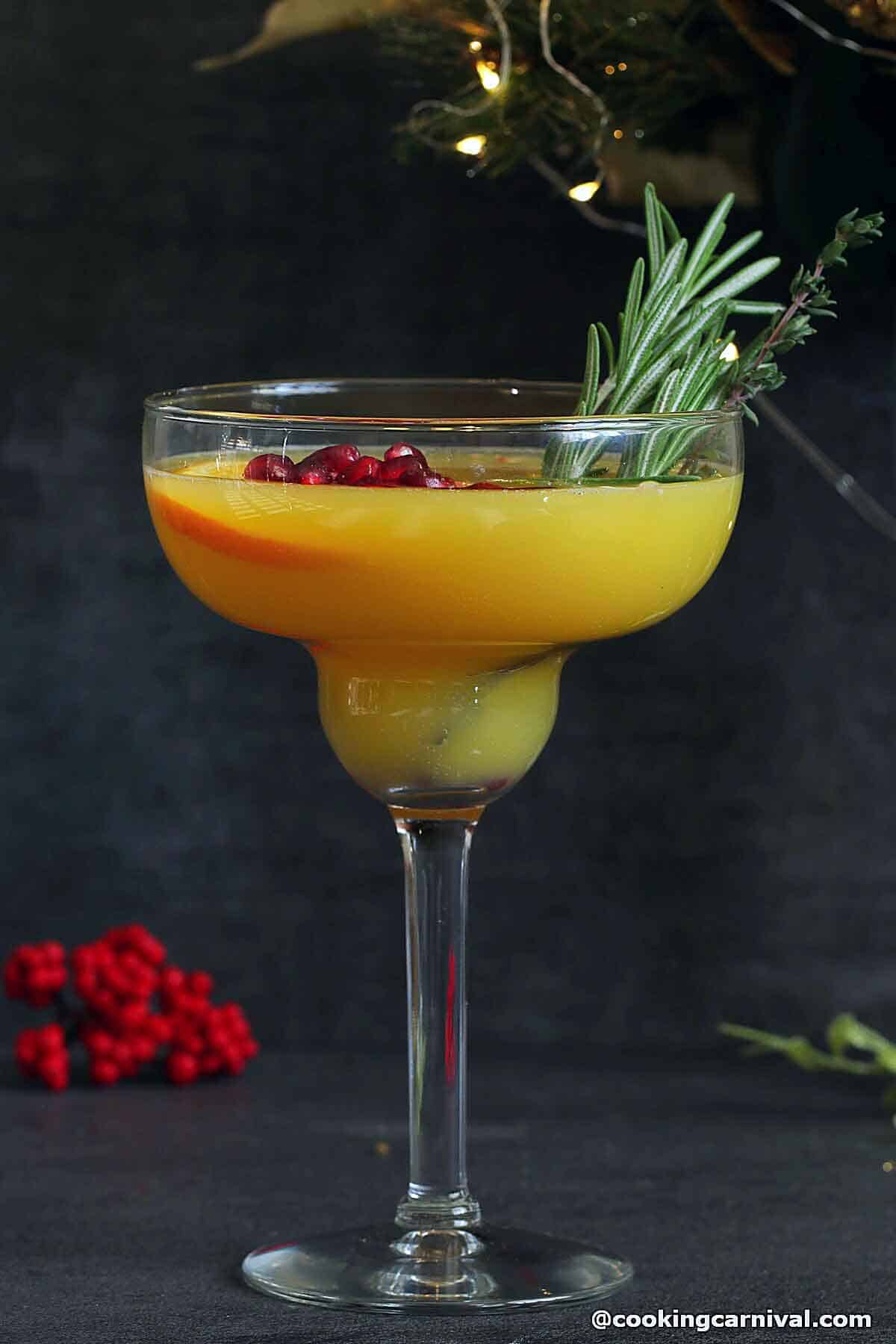 Orange mocktail in a glass garnished with rosemary and thyme.