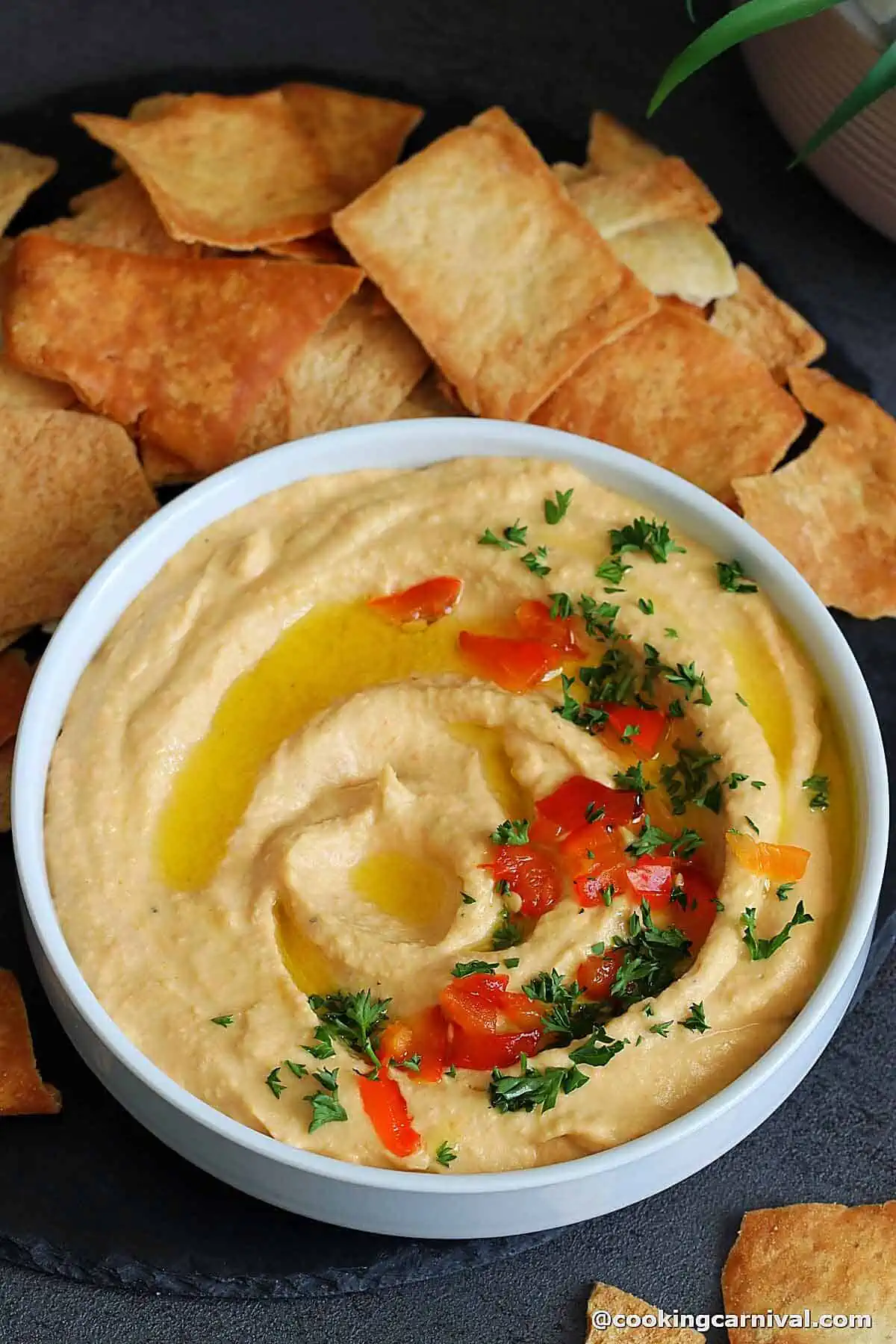 Roasted red pepper hummus in a bowl, topped with olive oil and parsley.