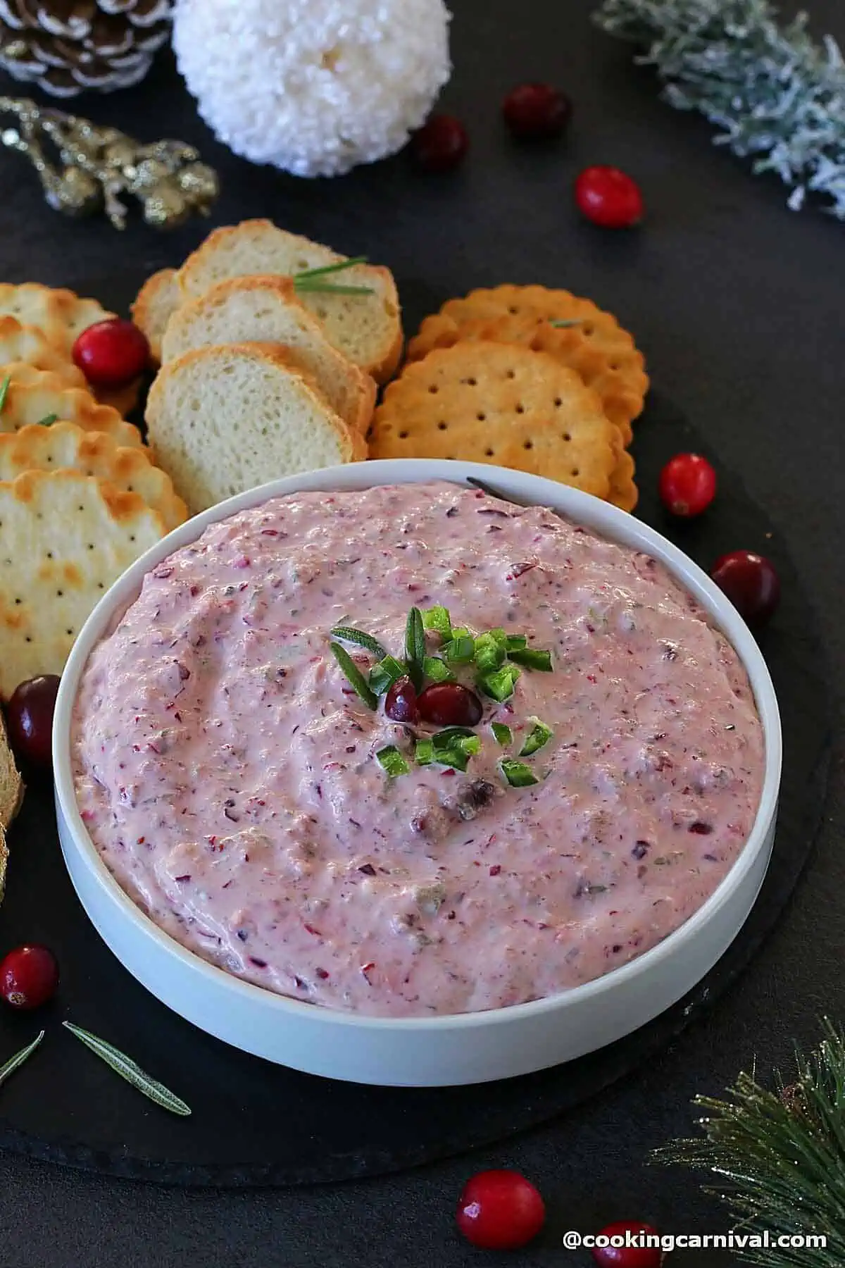 Cranberry jalapeno dip is served in a white dipping bowl with crackers and crostini.