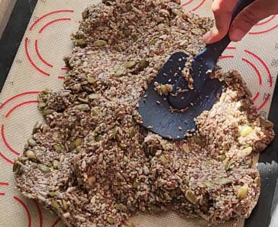 spreading 6 seeds cracker mixer on a baking sheet.