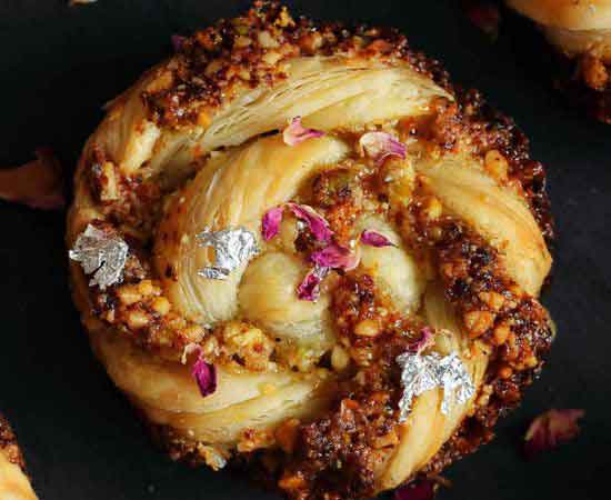 baking puff pastry swirl gujiya garnished with silver varq and rose petals.