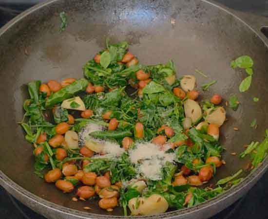 adding salt in sauted moringa, cilantro, green chili, garlic, and peanut